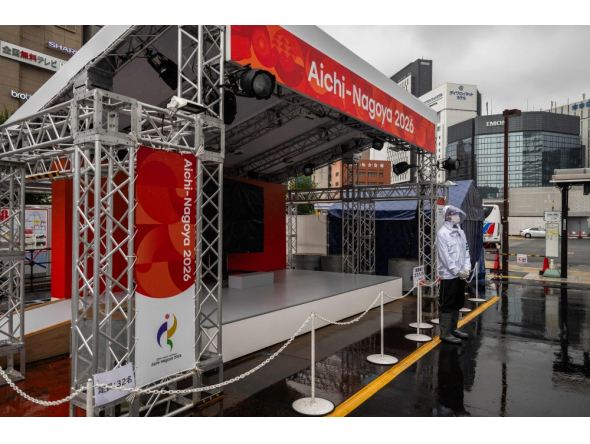 A man wearing a rain jacket stands in front of a booth promoting the 2026 Asian Games in Nagoya, Aichi Prefecture on September 16, 2026. (Photo by Mohd Rasfan / AFP)