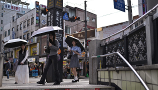 People shield themselves with umbrellas while walking past the metro station entrance in Jongno 3-ga in Seoul on September 20, 2026. (Photo by Lillian SUWANRUMPHA / AFP)