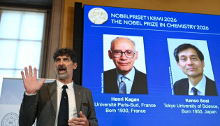 The chair of the Nobel Committee for Chemistry Heiner Linke (L) explains the field of research of Nobel Prize winners France's Henri Kagan and Japan's Kenso Soai (displayed on the screen in background) during a press conference in Stockholm, Sweden, on October 7, 2026. (Photo by Jonathan Nackstrand / AFP)