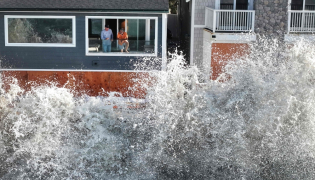 In an aerial view, people watch from a home as a Pacific Ocean wave crashes into a seawall protecting homes amid powerful surf on October 9, 2026 in Long Beach, California. (Photo by Mario Tama/Getty Images/AFP ) 