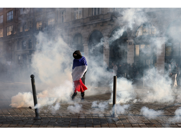 A protester, wrapped in a flag of France, stands in the smoke at Place de l'Opera during ongoing protest action, in Lille, northern France, on October 17, 2026. (Photo by Sameer Al-Doumy / AFP)