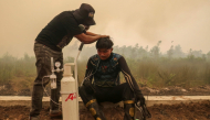 This picture taken on October 22, 2026 shows a volunteer from the Central Kalimantan Forest and Land Fire Smoke Response Coalition (RAKAT) providing mobile oxygen relief to a firefighter while battling forest and land fires in Palangkaraya, Central Kalimantan. (Photo by REINA / AFP)