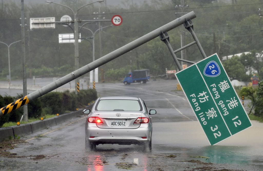 A car drives pass a collapsed traffic sign, toppled by strong winds of typhoon Meranti, as it slashes southern Taiwan on September 14, 2016.   AFP / SAM YEH