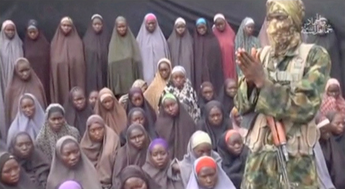 This video grab image created on August 14, 2016 taken from a video released on youtube purportedly by Islamist group Boko Haram showing what is claimed to be one of the groups fighters at an undisclosed location standing in front of girls allegedly kidna