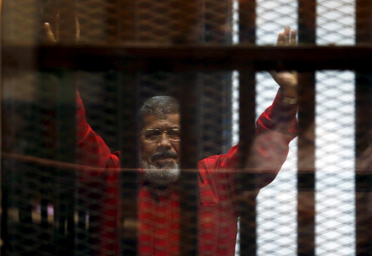 Egypt's deposed president Mohamed Mursi greets his lawyers and people from behind bars at a court wearing the red uniform of a prisoner sentenced to death, during his court appearance with Muslim Brotherhood members on the outskirts of Cairo, Egypt, on Ju