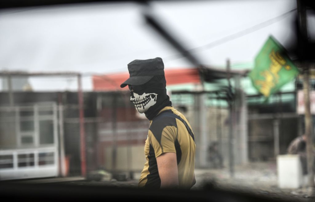 A member of Iraqi forces, wearing a skull mask, waits at a checkpoint for people fleeing the main hub city of Mosul on October 28, 2016 between Qayyarah and Mosul during an operation to retake the city from the Islamic State (IS) group. AFP / BULENT KILIC