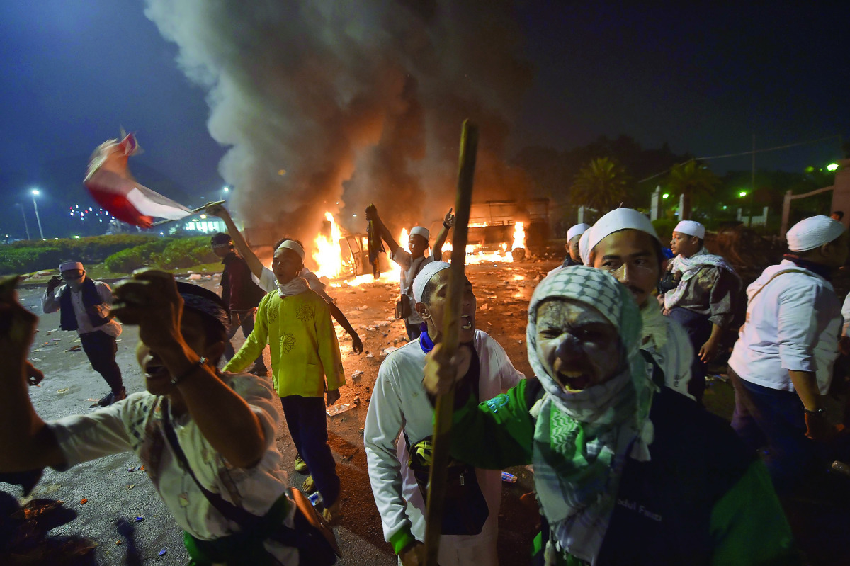 Indonesian protesters react as police shoot tear gas next to two burned cars outside the presidential palace in clashes that marred an otherwise peaceful rally against governor Basuki Tjahaja Purnama, a Christian accused of insulting Islam, in Jakarta on 