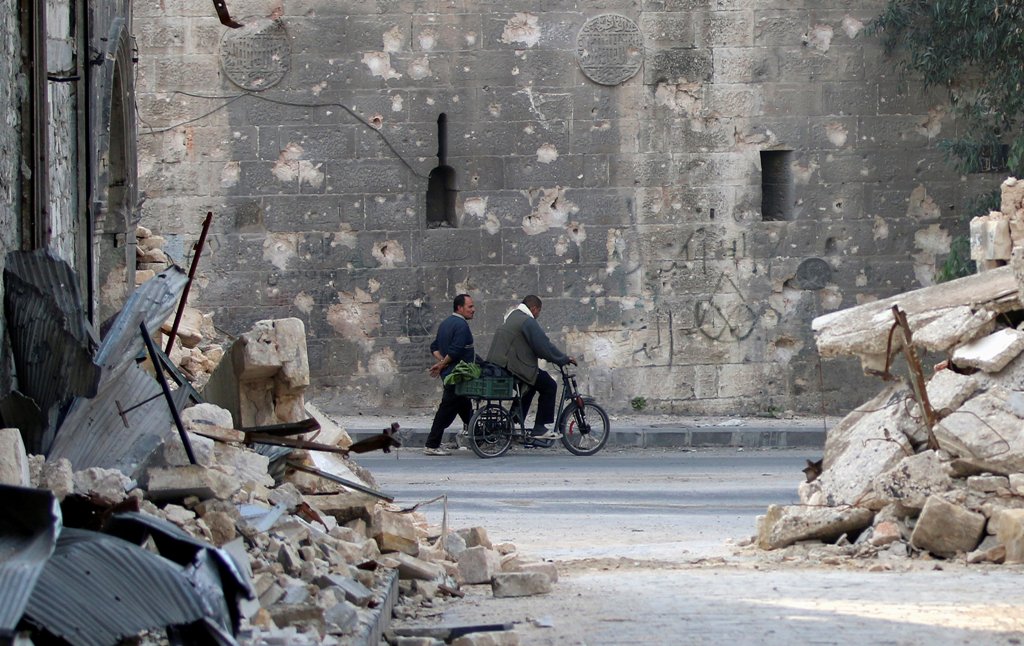 A man walks past a man riding a bike near the rubble of damaged buildings in the rebel held area of Old Aleppo, Syria November 14, 2016. REUTERS/Abdalrhman Ismail
