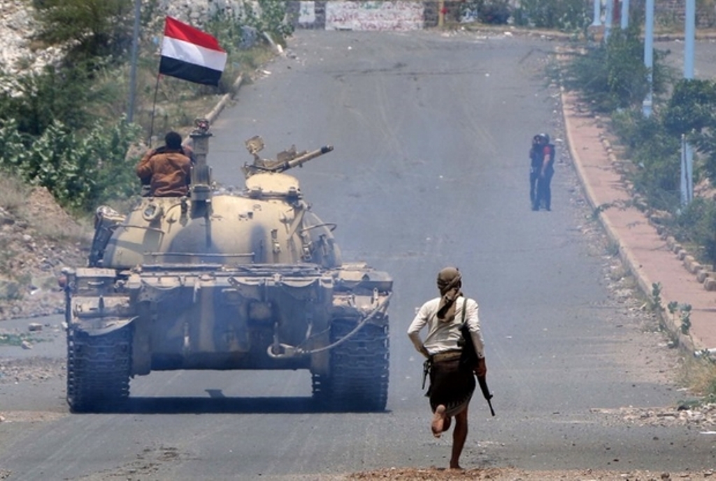 A fighter loyal to Yemen's exiled President Abd Rabbuh Mansour Hadi runs behind a tank near the city of Taiz on 7 September 2016 (AFP)