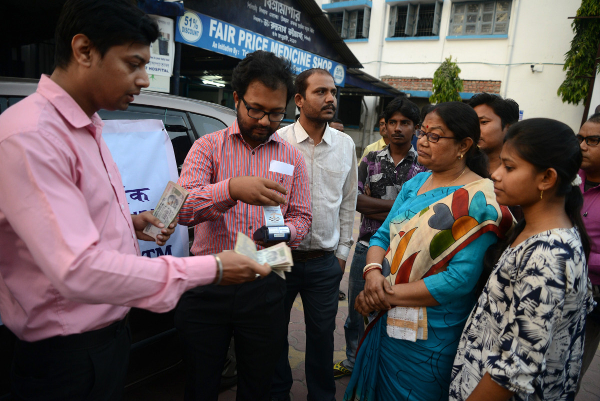 Indian banking staff of the State Bank of India assist customers to withdraw money with the use of a mobile banking machine at Siliguri District hospital in Siliguri on November 22, 2016. Prime Minister Narendra Modi sent shockwaves through the country by