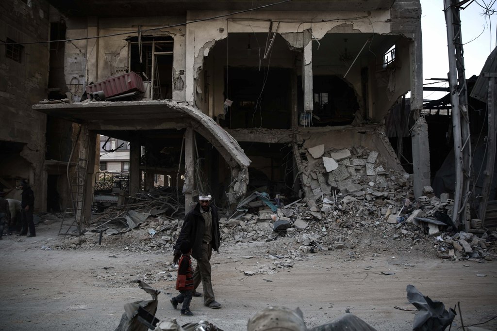  An injured Syrian man walks with his son past a destroyed building on November 22, 2016, in the rebel-held town of Douma, on the eastern outskirts of the capital Damascus. / AFP / Sameer Al-Doumy