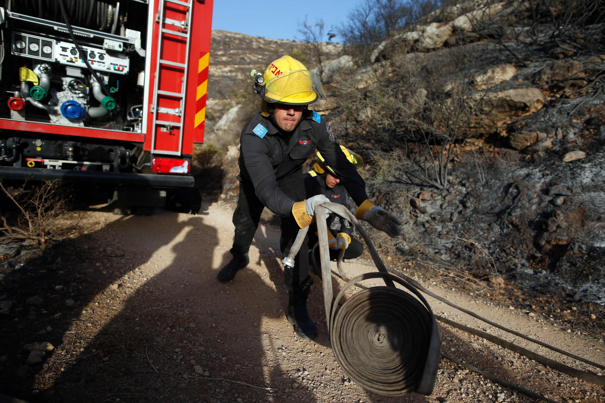 An Israeli firefighter unloads hose as they battle a fire in the village of Nataf close to Jerusalem, as it continues to spread in the area, on November 26, 2016. Wildfires near Jewish settlements in the occupied West Bank have forced hundreds to flee the