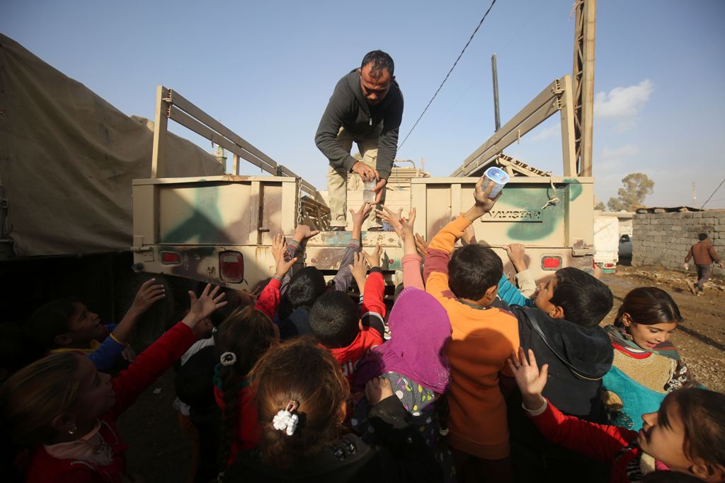 An Iraqi soldier distributes drinks and food to Iraqi children, displaced from the outskirts of the city of Tal Afar, arrive on trucks on December 3, 2016 in the village of Tall al-Zarka after their families fled the ongoing fighting between Iraqi forces 