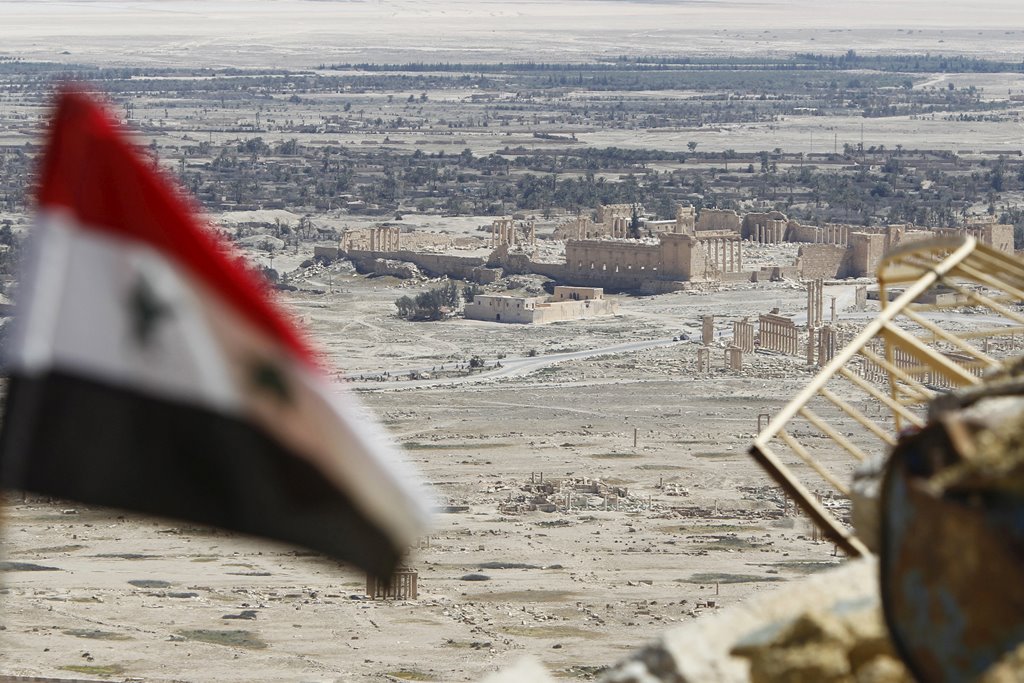 A Syrian national flag flutters as the ruins of the historic city of Palmyra are seen in the background, in Homs Governorate, Syria April 1, 2016. REUTERS/Omar Sanadiki/File Photo