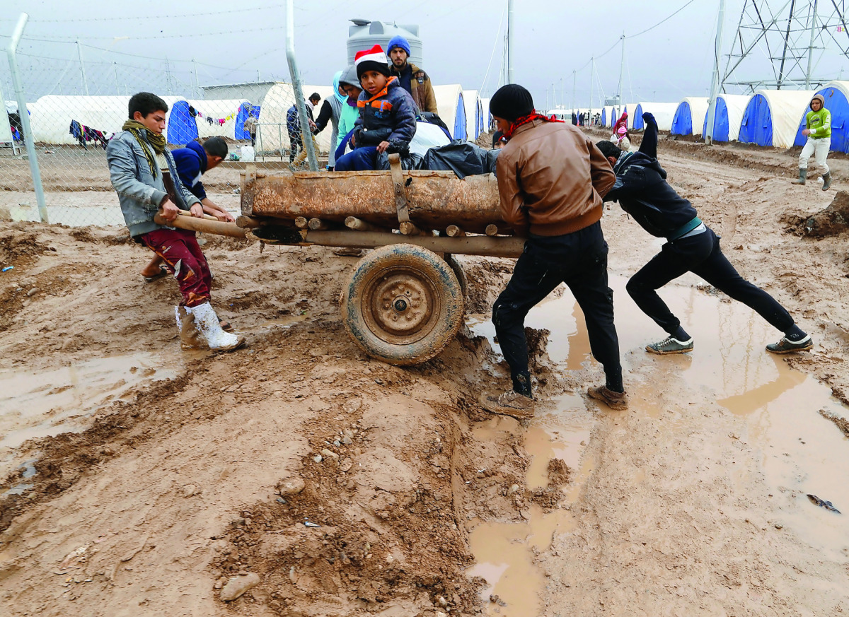 Displaced Iraqis who fled the Islamic State stronghold of Mosul, push a cart through mud following heavy rain at Khazer camp, yesterday.
