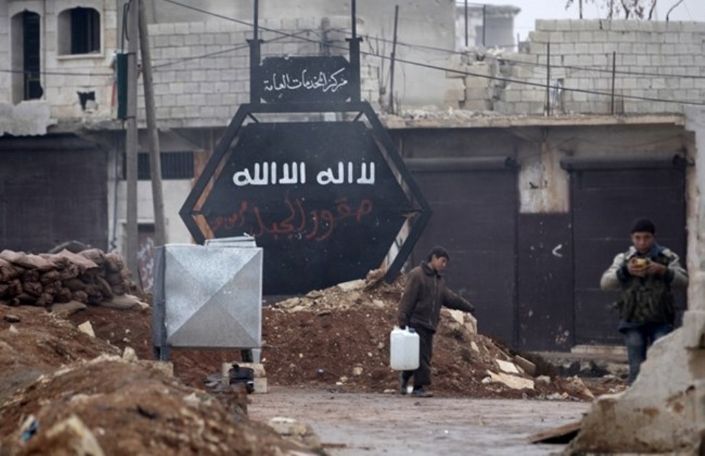 A boy carries a water container near a sign that used to belong to ISIS in al-Rai town, northern Aleppo countryside, Syria December 25, 2016. (REUTERS/Khalil Ashawi).