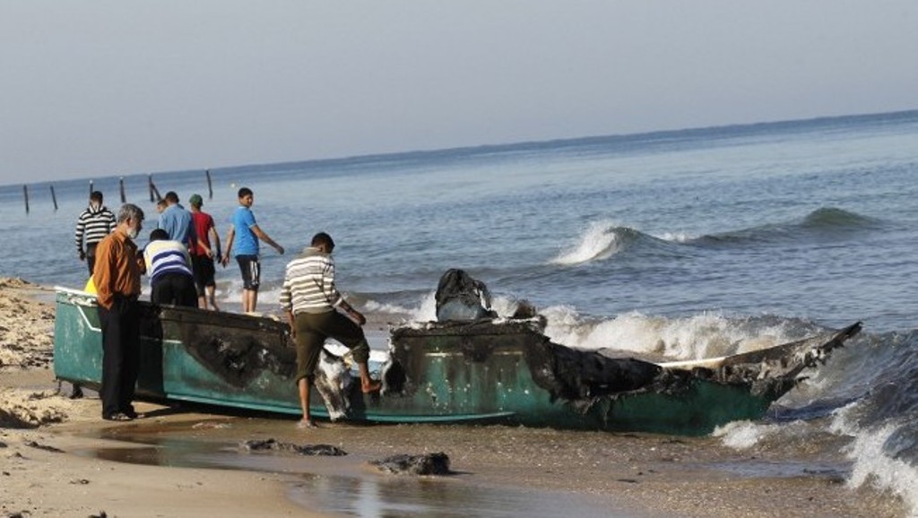 Palestinian fishermen inspect their destroyed fishing boat hauled up onto the shore, close to the southern Gaza Strip town of Rafah, on March 26, 2014. Several Palestinians were wounded when Israeli navy vessels shot at two Gaza-bound boats smuggling ciga