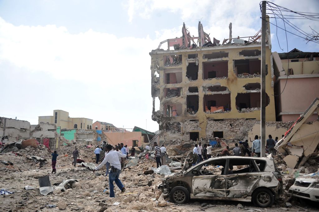 People react and walk among rubbles following an attack outside an hotel on January 25, 2017, in Mogadishu. At least seven people were killed after two car bombs exploded outside a popular Mogadishu hotel and gunmen forced their way inside the building an