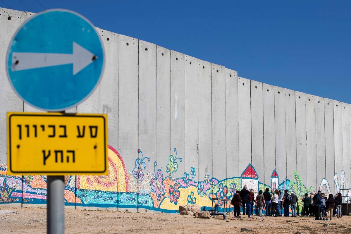 Israeli tourists take pictures of graffiti on part of Israeli controversial separation barrier in the Israeli Kibbutz of Netiv Haashara along the border between Israel and the Gaza Strip on February 7, 2017. AFP / Jack Guez