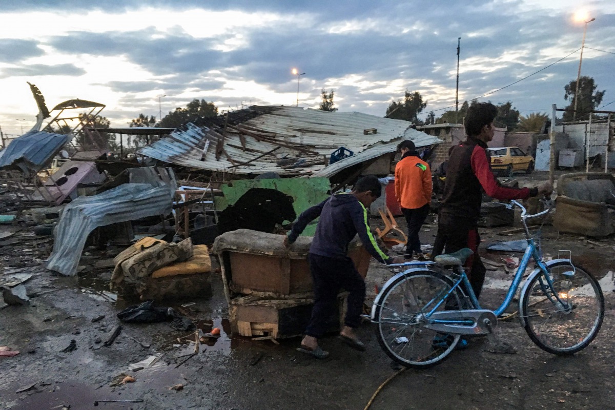 A picture taken with a mobile phone on February 16, 2017 shows two Iraqi children walking with a bicycle at the scene of a blast by a massive car bomb which killed dozens in a used car market in southern Baghdad. The Amaq propaganda agency linked to the I