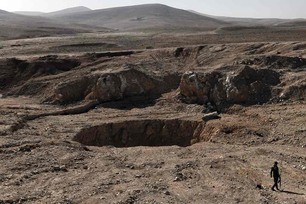 A member of the Hashed al-Shaabi (Popular Mobilisation) paramilitaries, walks next to a sinkhole, known as the Khasfah (an Arabic word for a crack or a hole that opens up in the ground), in the village of Athbah, south of Mosul on February 26, 2017. / AFP