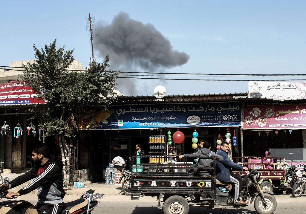 Palestinians drive on a road as smoke billows, in the background, following an Israeli airstrike on Rafah, in the southern Gaza Strip on February 27, 2017. / AFP / SAID KHATIB