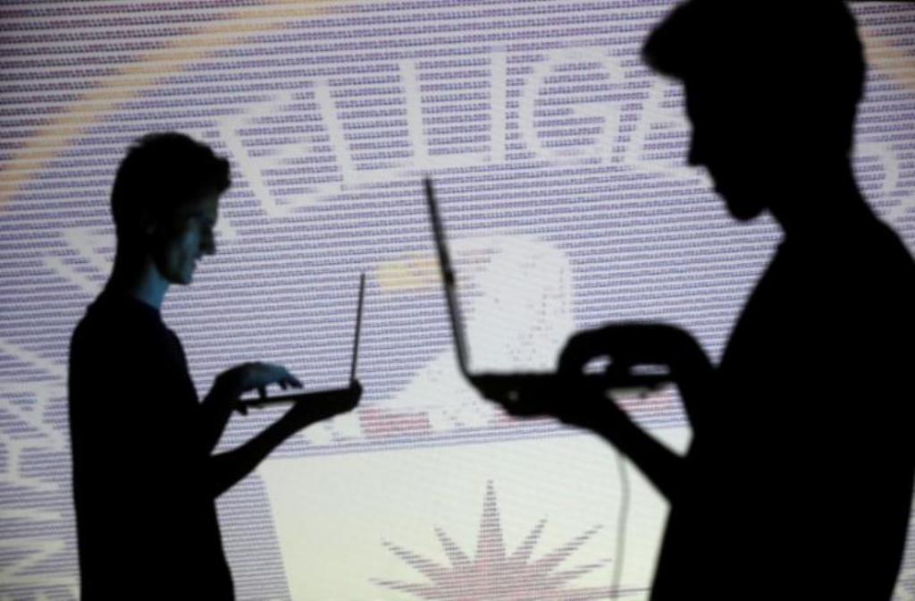 People are silhouetted as they pose with laptops in front of a screen projected with binary code and a Central Inteligence Agency (CIA) emblem, in this picture illustration taken in Zenica, Bosnia and Herzegovina October 29, 2014. REUTERS/Dado Ruvic/File 