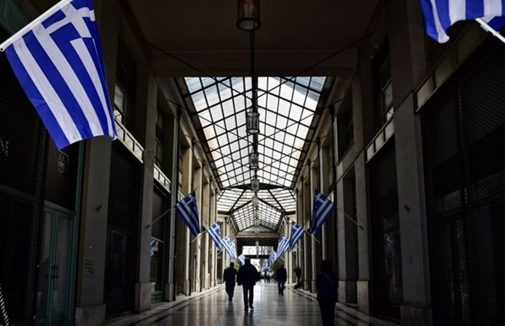Men walk in a passage adorned with Greek flags in central Athens on March 21, 2017. / AFP / LOUISA GOULIAMAKI.