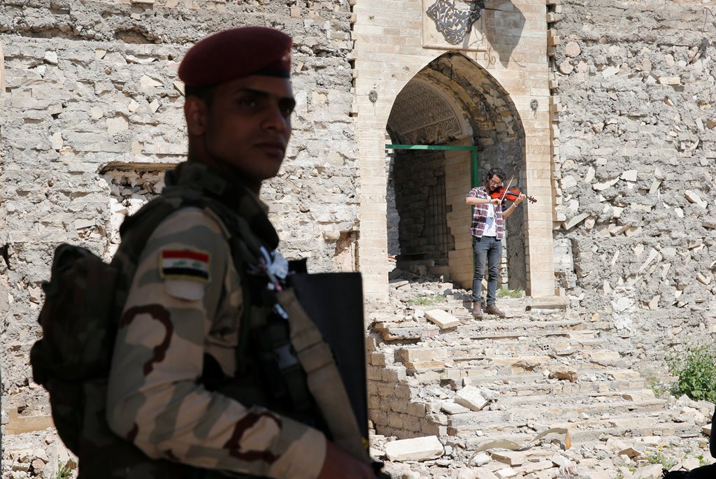 A member of the Iraqi security stands guard as Ameen Mukdad (R), a violinist from Mosul who lived under ISIS's rule for two and a half years where they destroyed his musical instruments, performs at Nabi Yunus shrine in eastern Mosul, Iraq, April 19, 2017