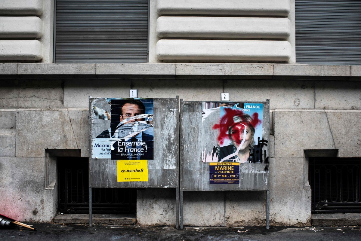 A picture shows vandalised campaign posters of French presidential candidates Emmanuel Macron (L) of the En Marche ! movement and Marine Le Pen (R) of the far-right National Front (FN) in Lyon on May 1, 2017 ahead of the second and final round of the Fren
