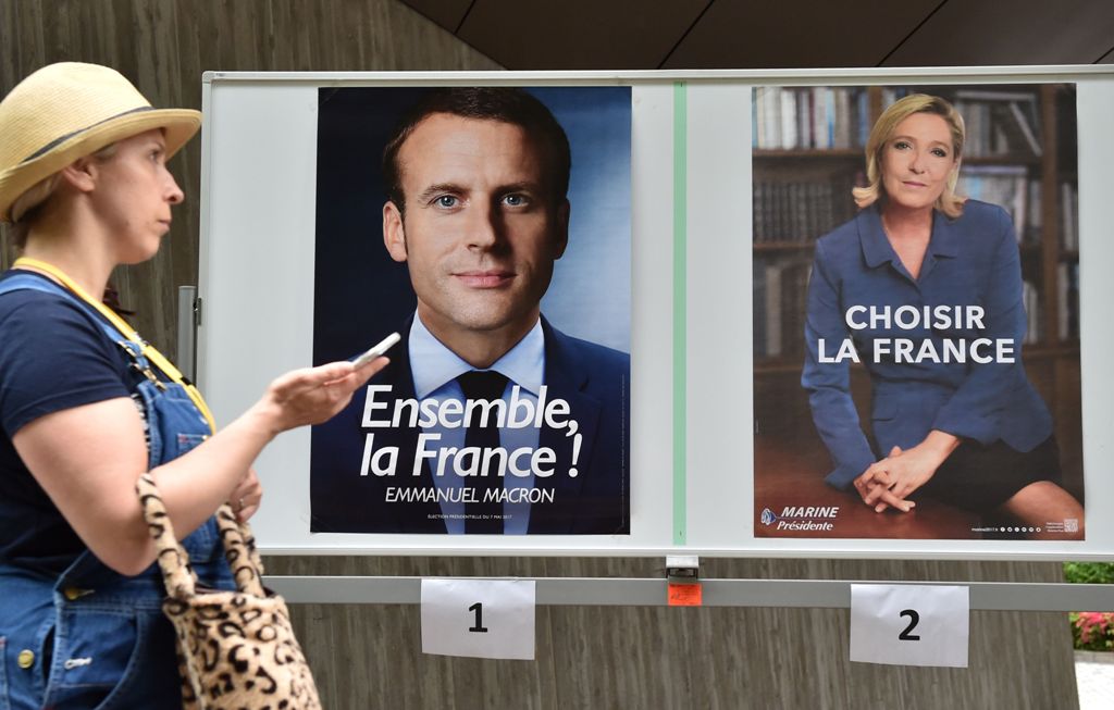 A woman walks past portraits of French presidential candidates, former economy minister Emmanuel Macron (L) and far-right National Front leader Marine Le Pen (R), after her voting at a polling station at the French embassy in Tokyo on May 7, 2017. / AFP.