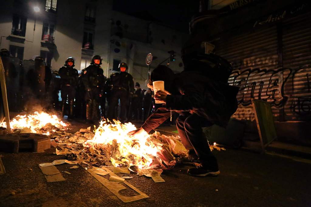 Riot police stand in front of a youngster gesturing near papers set on fire in Menilmontant district of Paris during the night on May 7, 2017 after the announcement of the French presidential election results. / AFP / Lara Priolet.