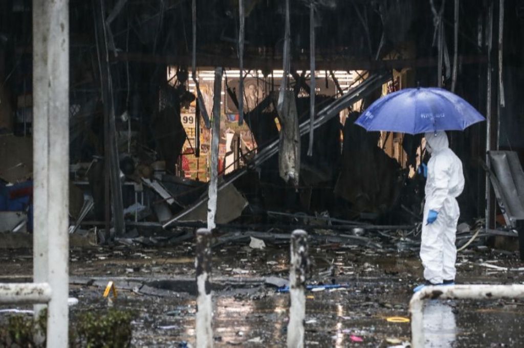 A Thai forensics worker shields himself with an umbrella whilst inspecting the aftermath of a bomb attack in the town centre of Pattani on May 9, 2017 (AFP Photo/TUWAEDANIYA MERINGING).