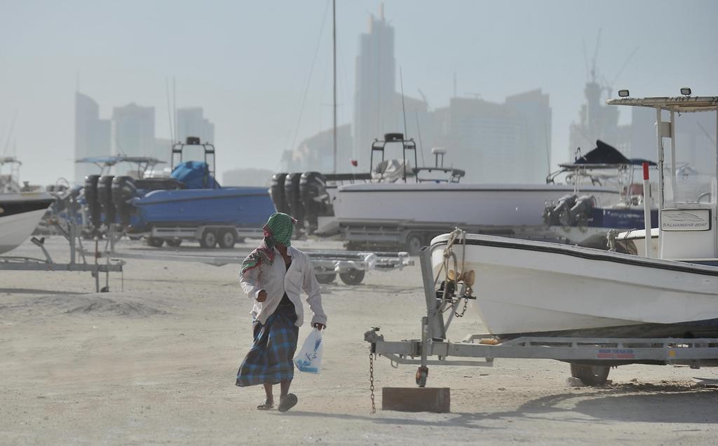 Man covering his face from the dust while walking through wave of  dusty winds at Doha corniche harbor Yesterday.  Baher Amin © The Peninsula