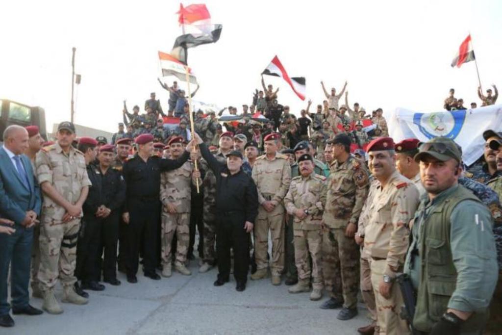 Iraqi Prime Minister Haider al-Abadi (C) holds an Iraqi flag as he announces victory over Islamic State in Mosul, Iraq, July 10, 2017. Iraqi Prime Minister Media Office/Handout via REUTERS.