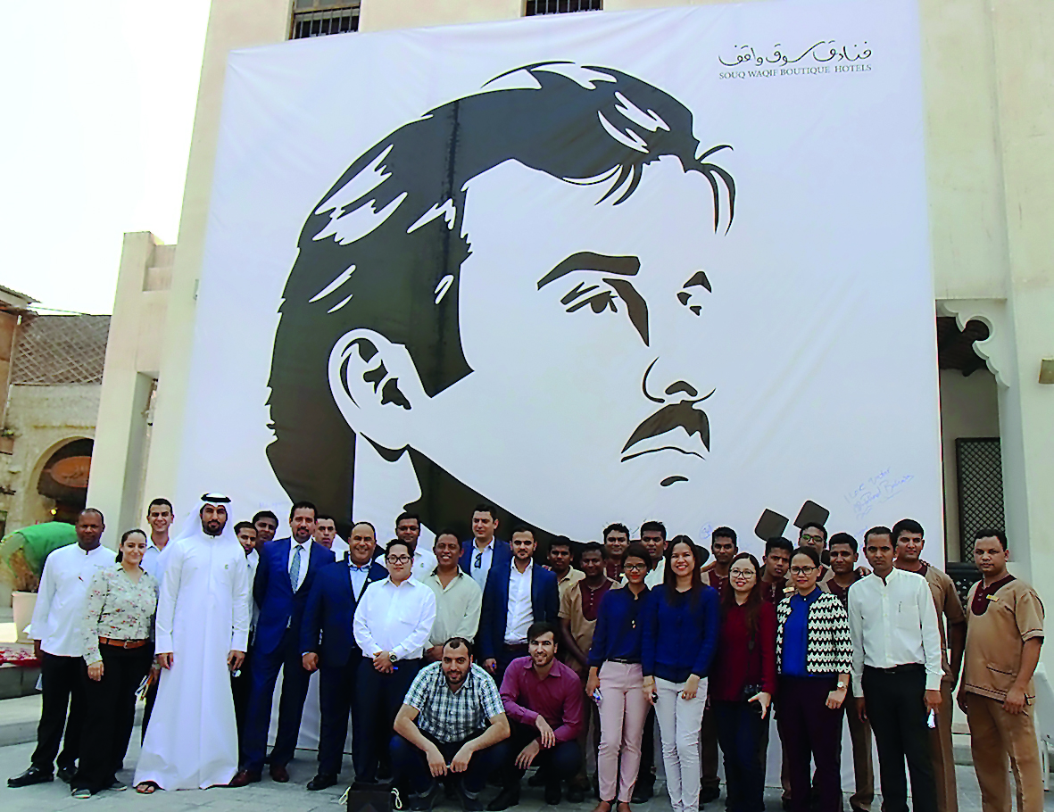 The management and staff of Souq Waqif Boutique Hotels in front of the mural of Emir H H Sheikh Tamim bin Hamad Al Thani. 