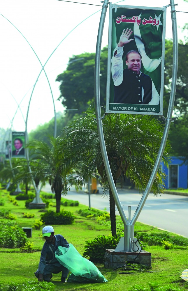 A worker cleans a garden under a billboard with the portrait of Pakistani Prime Minister Nawaz Sharif along a street, in Islamabad, yesterday.