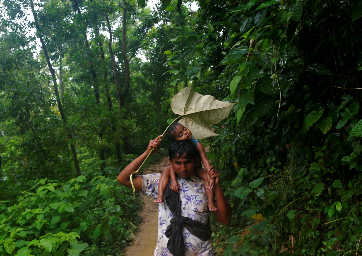 A Rohingya refugee man protects his sister from rain as he climbs down a hill after crossing the Bangladesh-Myanmar border in Cox's Bazar, Bangladesh September 8, 2017. Reuters/Danish Siddiqui

