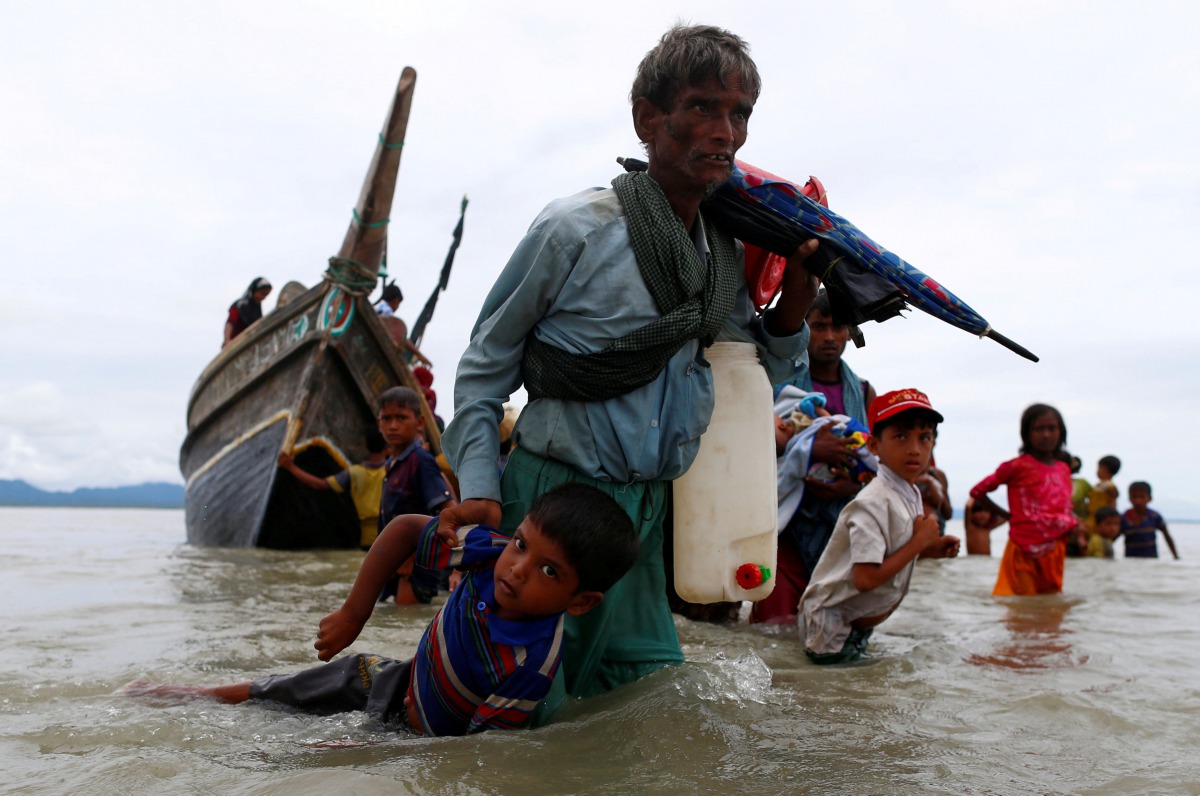 A Rohingya refugee man pulls a child as they walk to the shore after crossing the Bangladesh-Myanmar border by boat through the Bay of Bengal in Shah Porir Dwip, Bangladesh, September 10, 2017. Reuters/Danish Siddiqui