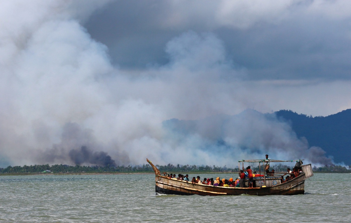 Smoke is seen on Myanmar's side of border as a boat carrying Rohingya refugees arrives on shore after crossing the Bangladesh-Myanmar border through the Bay of Bengal, in Shah Porir Dwip, Bangladesh September 11, 2017. Reuters/Danish Siddiqui
