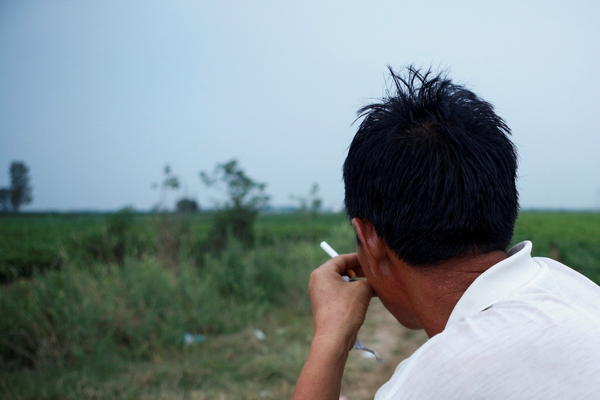 Zheng Xianqiao, the father of the student Zheng Dexing, who committed suicide after accumulating crippling debt, sits near his son's grave on a farm in Dengzhou, Henan province, China, July 15, 2017. Reuters/Shu Zhang
