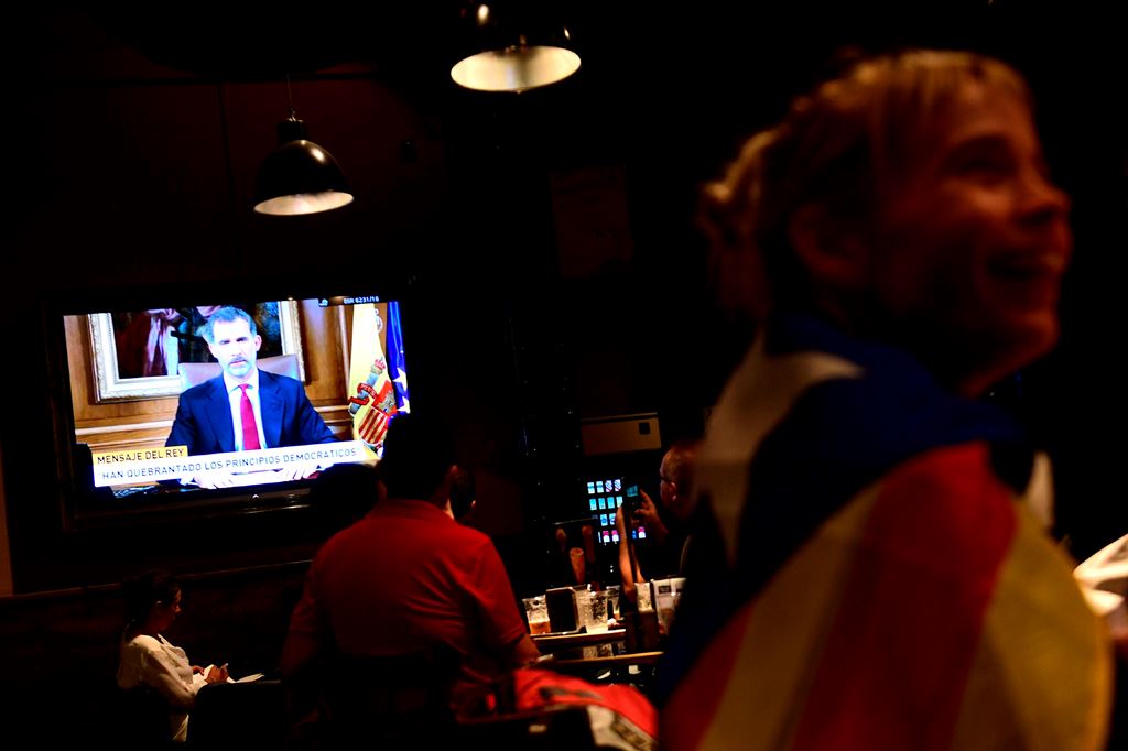 A woman wrapped in a Catalan pro-independence 'Estelada' flag listens to Spain's King Felipe VI address to the nation on a television set in a bar in Barcelona on October 3, 2017 during a general strike in Catalonia. AFP / PIERRE-PHILIPPE MARCOU