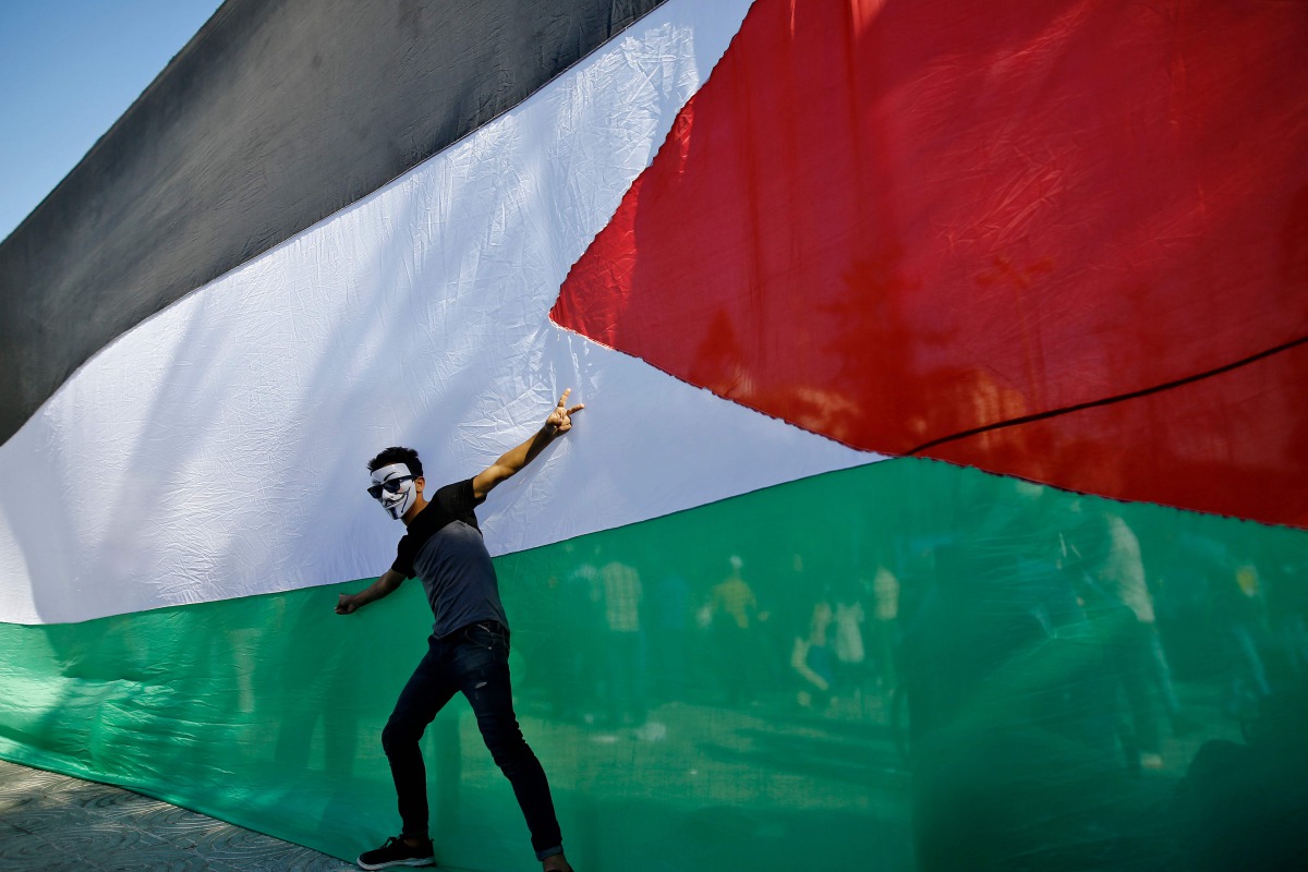 A Palestinian youth poses in front of his national flag during celebrations in Gaza City after rival Palestinian factions Hamas and Fatah reached an agreement on ending a decade-long split following talks mediated by Egypt on October 12, 2017.  AFP / Moha