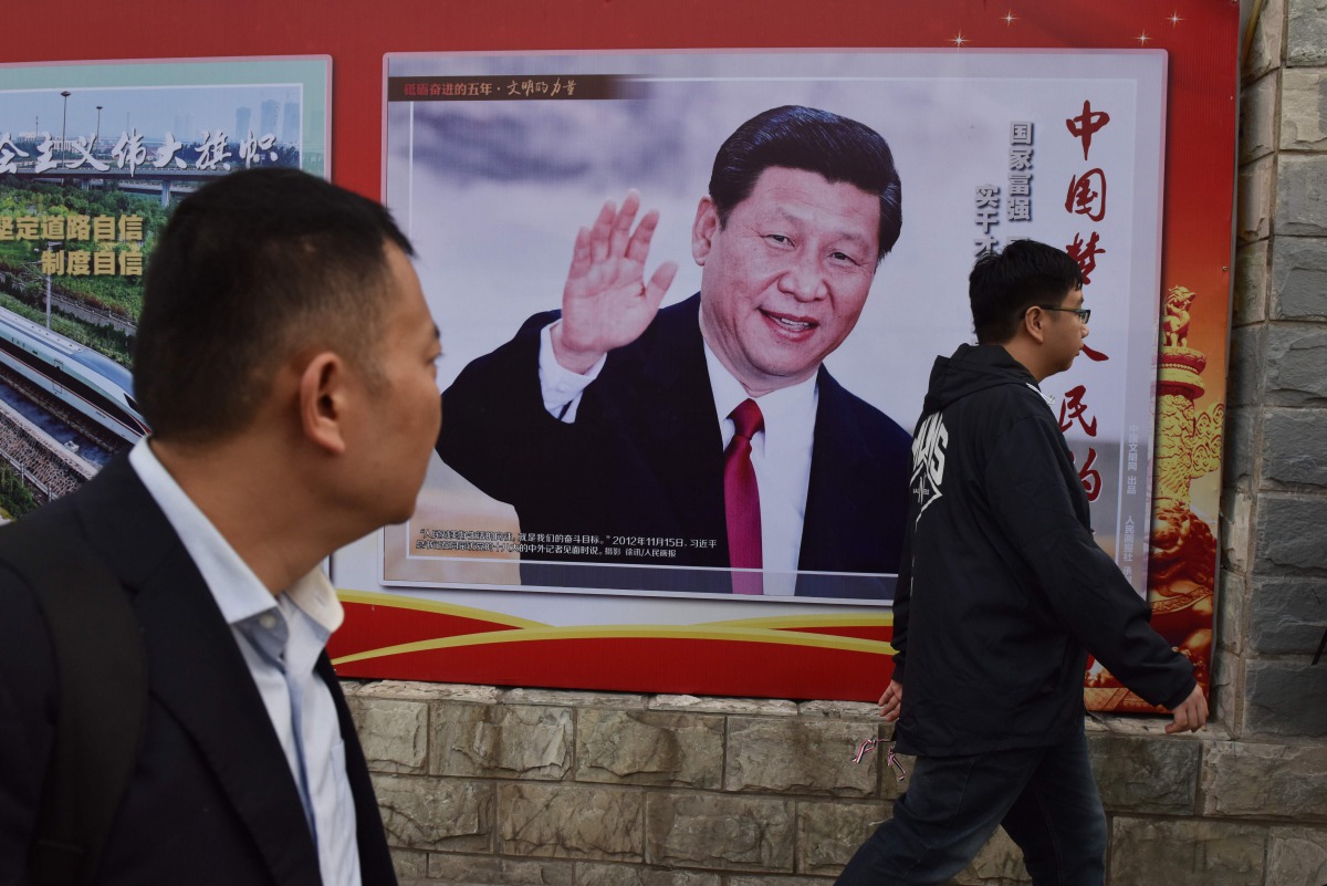 People walk past a poster featuring Chinese President Xi Jinping with a slogan reading 