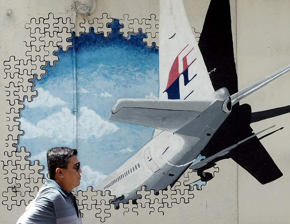(FILES) This file photo taken on March 8, 2016 shows a Malaysian man walking in front of a mural of missing Malaysia Airlines MH370 plane in a back-alley in Shah Alam.  AFP / MANAN VATSYAYANA
