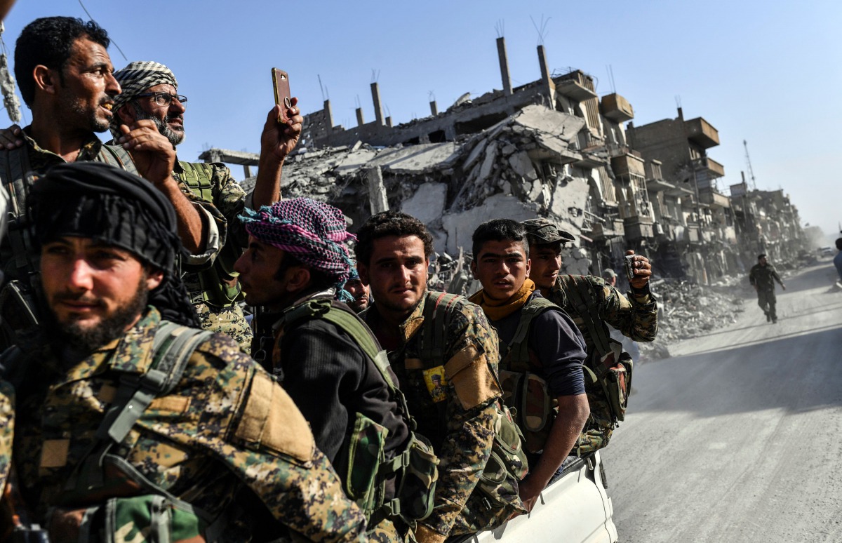 Kurdish fighters of the Syrian Democratic Forces (SDF) ride in the back of a truck passing damaged buildings in Raqa on October 20, 2017, after a Kurdish-led force expelled the Islamic State group from the northern Syrian city.  AFP / Bulent Kilic