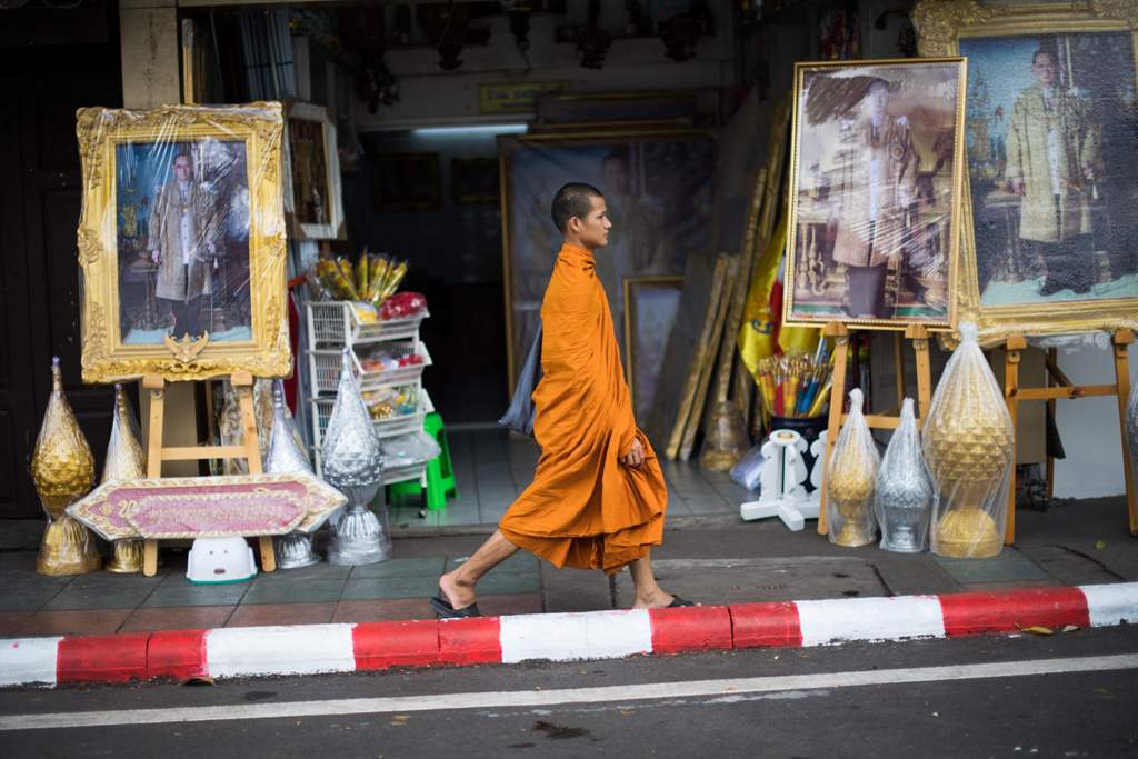 In this photograph taken on October 19, 2017, a Buddhist monk walks past framed images of Thailand's late king Bhumibol Adulyadej in front of a shop in Bangkok. The kingdom has been preparing for the cremation of the former king following his death at the