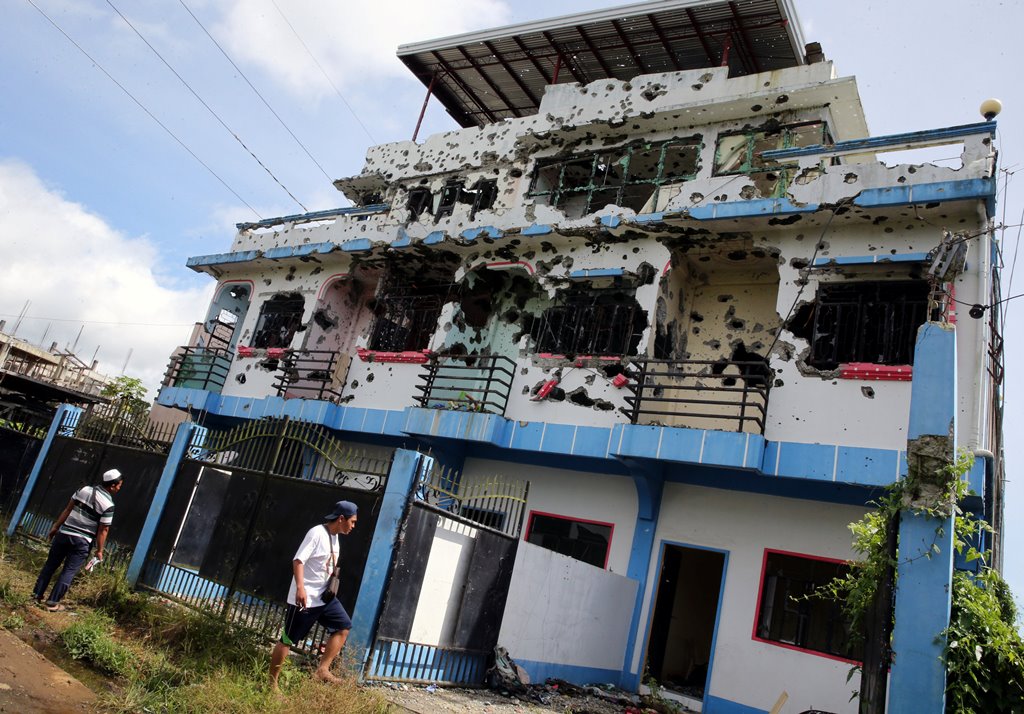 People walk in front of a bullet-riddled apartment house in a residential area in Malutlut district, Marawi city, southern Philippines October 27, 2017, which was believed to have been rented by pro-Islamic State militant group leaders Isnilon Hapilon and