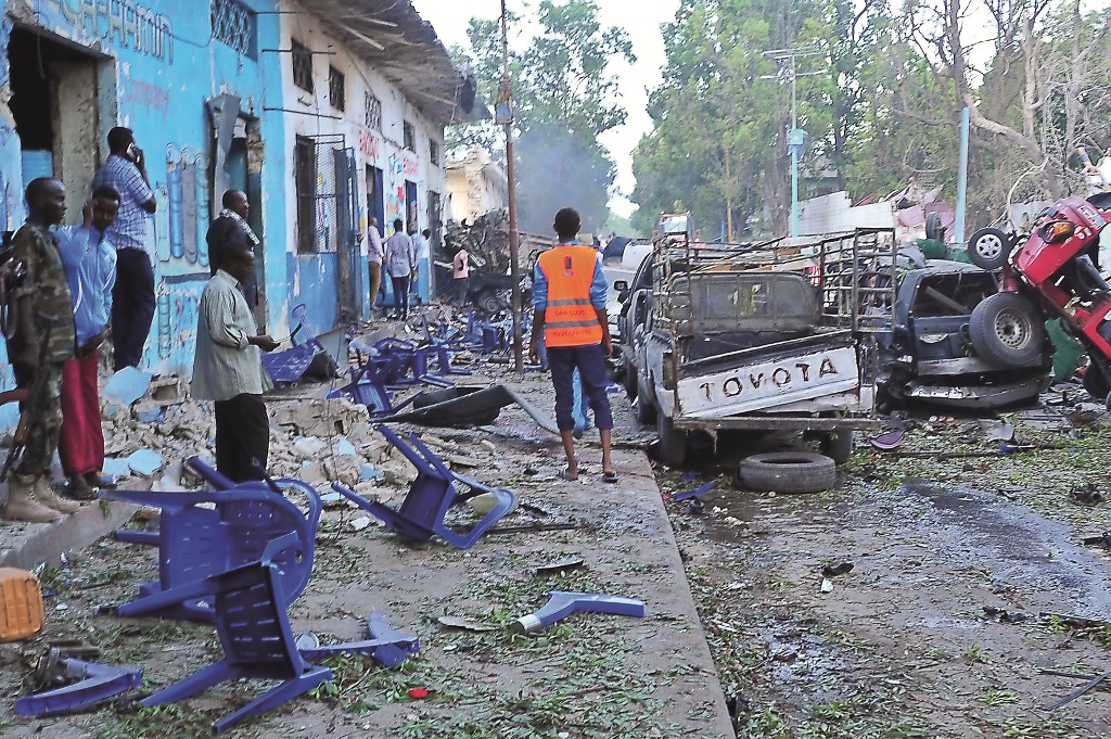A file photo of people standing among damages at the scene of a blast after two car bombs exploded in Mogadishu on October 28, 2017.  AFP / Mohamed ABDIWAHAB