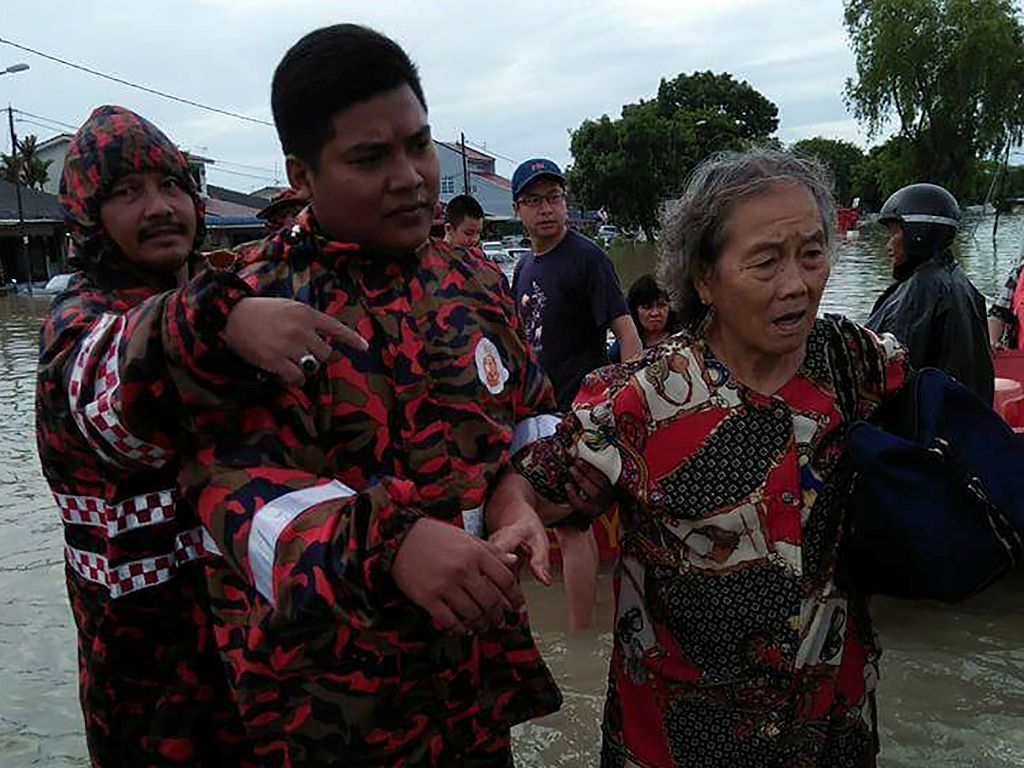 This handout photo from the Fire and Rescue Department of Malaysia taken and received on November 5, 2017 shows a rescue worker helping an elderly woman cross a flooded street in Bukit Mertajam, Penang. AFP
